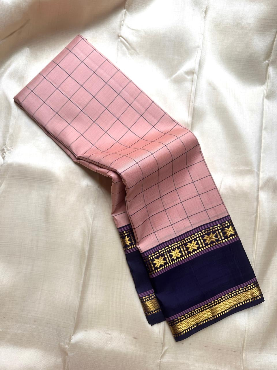 Draped blush pink checked pure Kanchipuram silk saree showing deep navy zari border with star motifs on a white fabric background