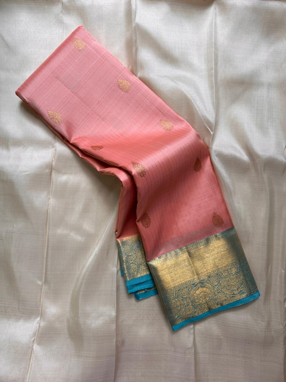 Blush pink pure Kanchipuram silk saree with gold paisley buttas and sky blue zari woven border, draped on light fabric