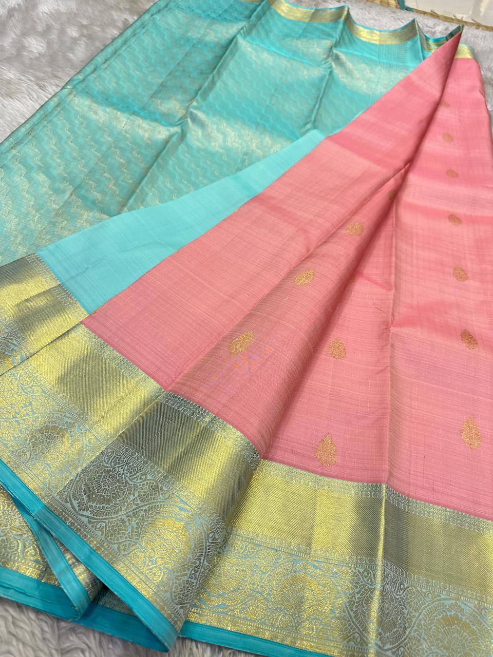Draped blush pink pure Kanchipuram silk saree showing small gold buttas and wide zari woven border with sky blue edging