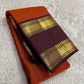 Brick red Kanchipuram saree folded showing deep maroon temple border