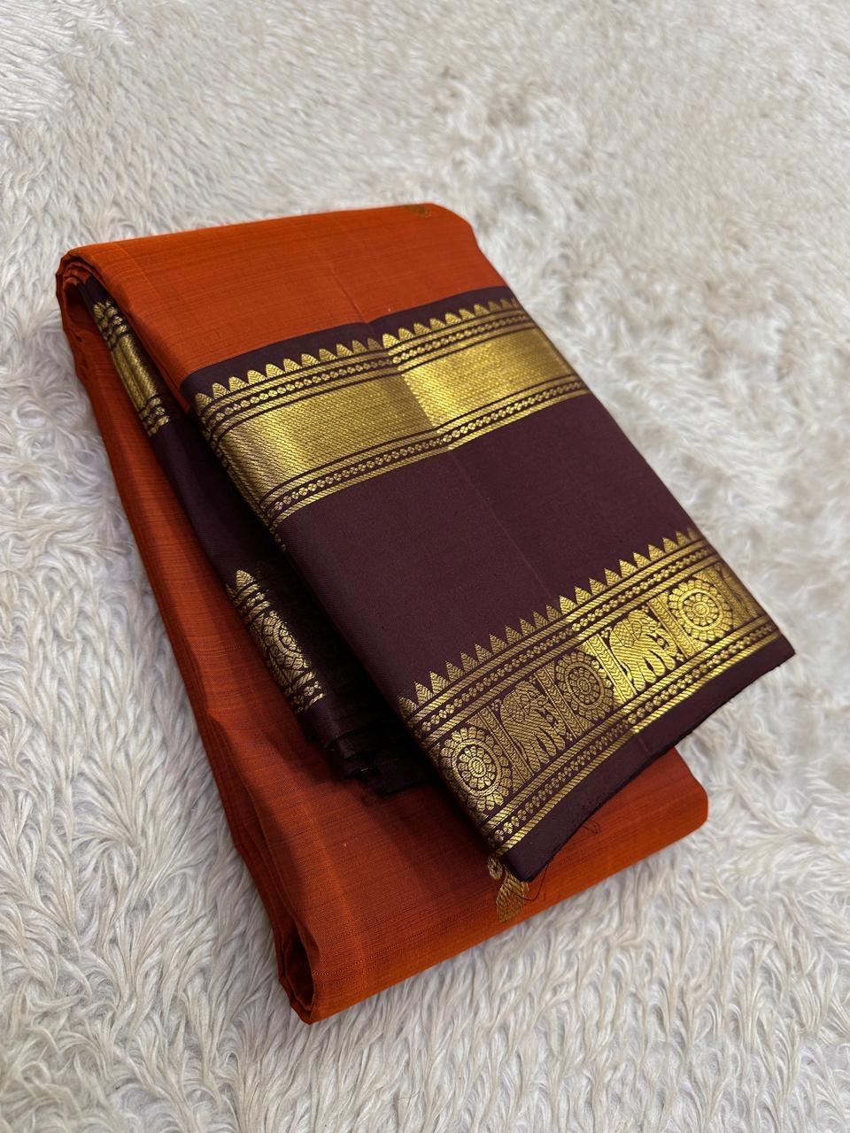 Brick red Kanchipuram saree folded showing deep maroon temple border