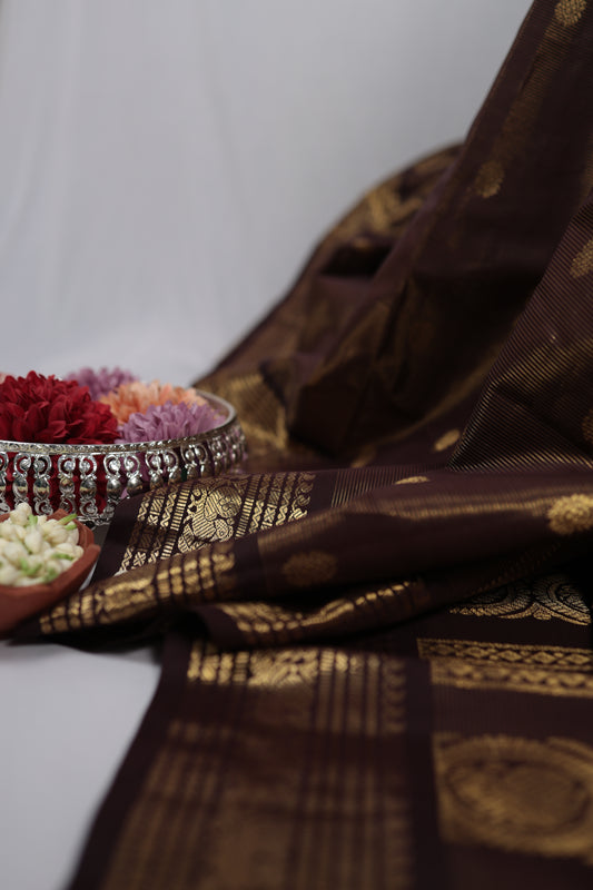 Deep brown vairaoosi Kanchipuram silk saree draped with zari woven border and flower bowl props
