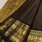 Detail of the saree border: A broad dark brown and antique-gold border with bold traditional figurative and geometric zari registers, finished with a narrow green edge.