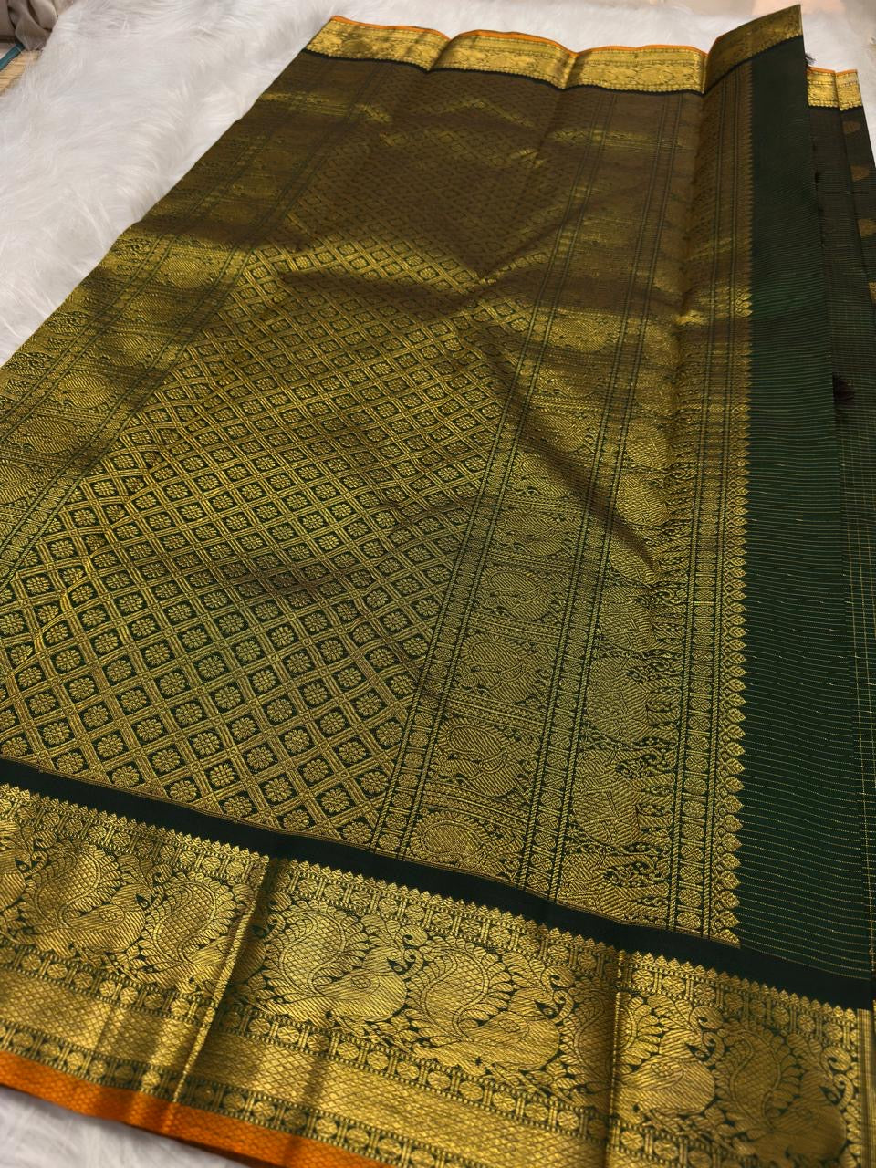 Burnished Orange selvedge finishing the Antique Gold zari border of the Deep Forest Green Kanchi Pattu saree.