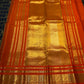 Burnt-orange Kanchipuram border with multiple classic-gold zari bands against the deep black checked body.