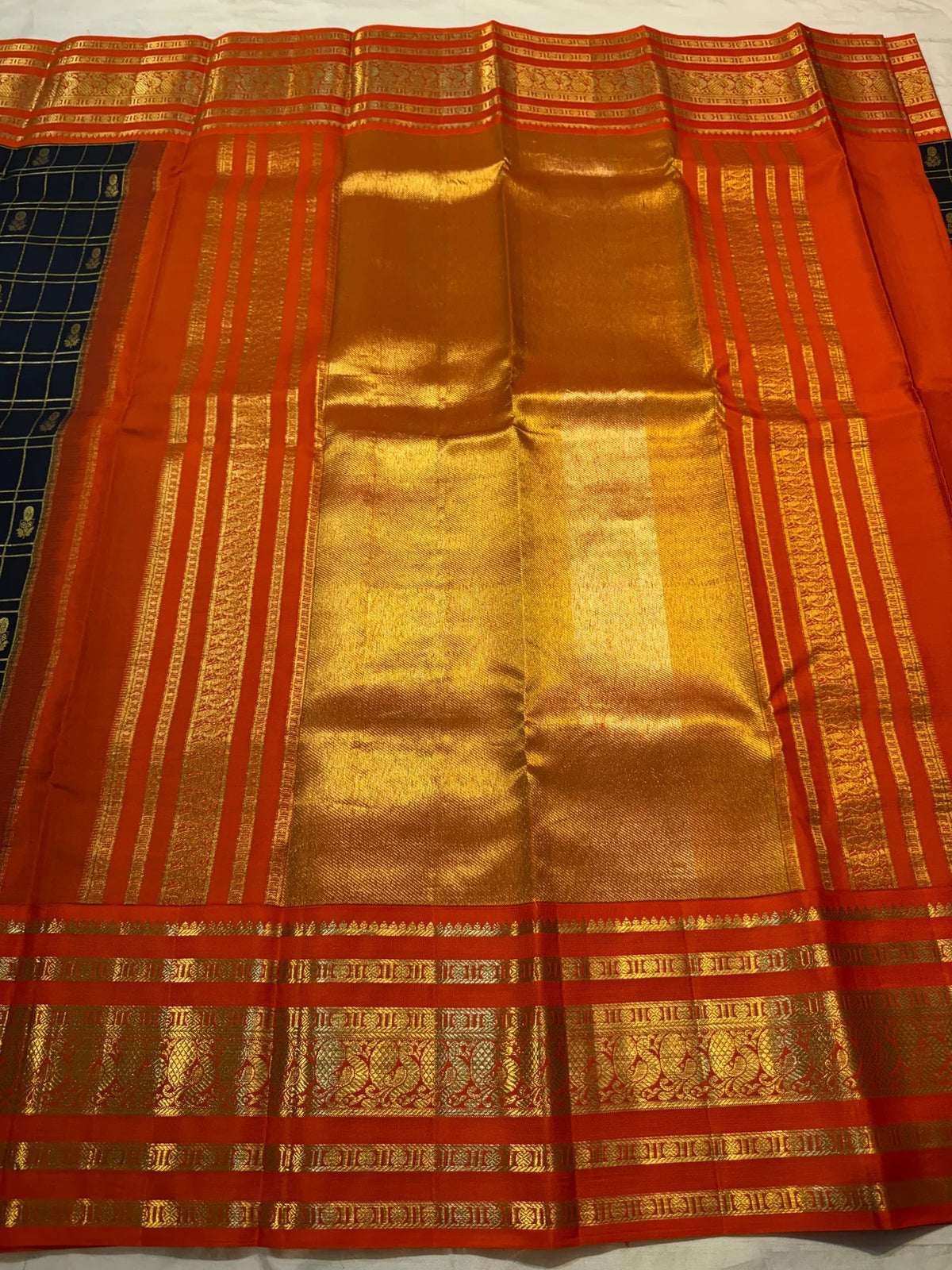 Burnt-orange Kanchipuram border with multiple classic-gold zari bands against the deep black checked body.