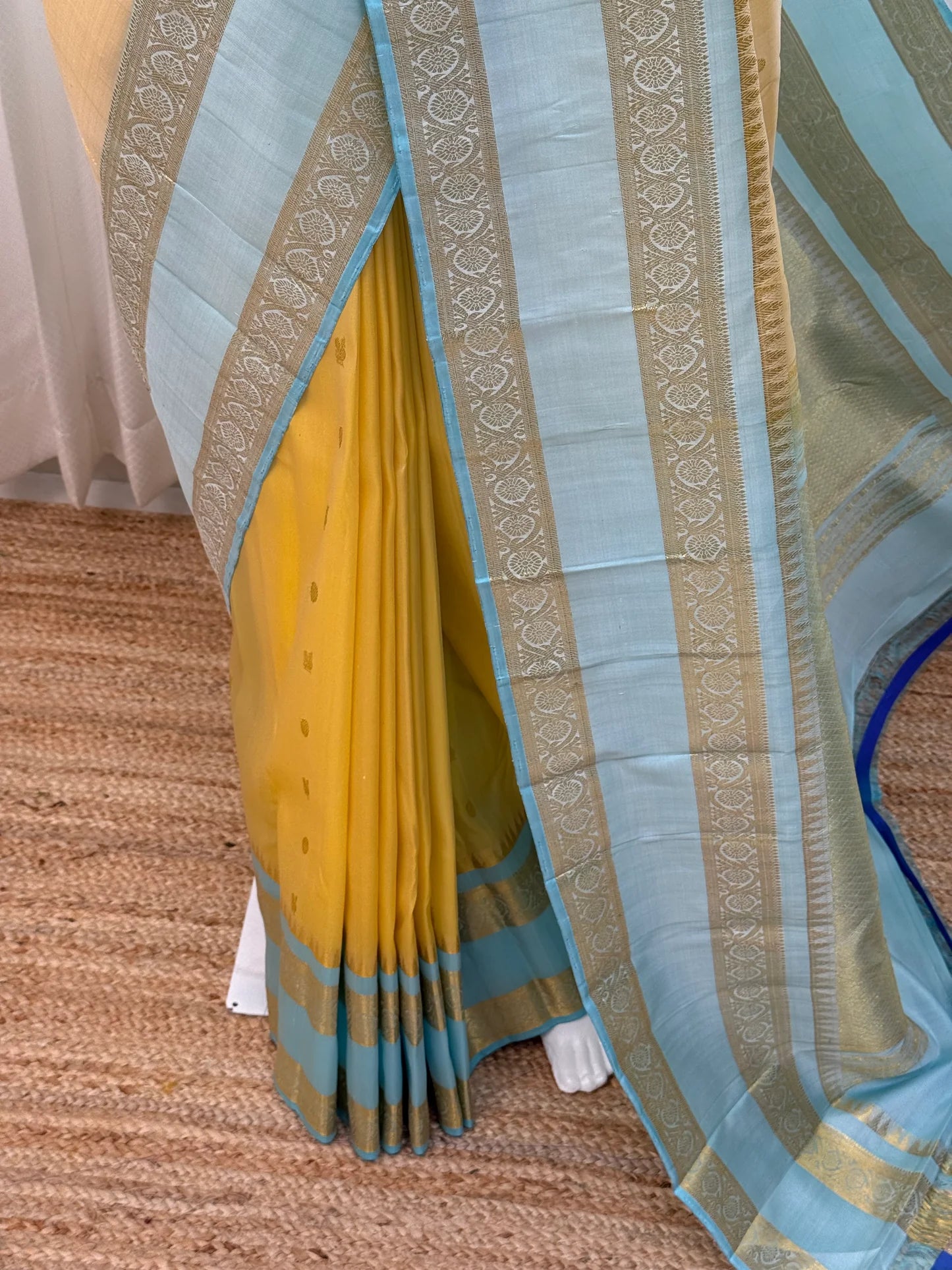 Pleated butter yellow Pure Kanchipuram silk saree showing sky blue border with wide zari woven motif band