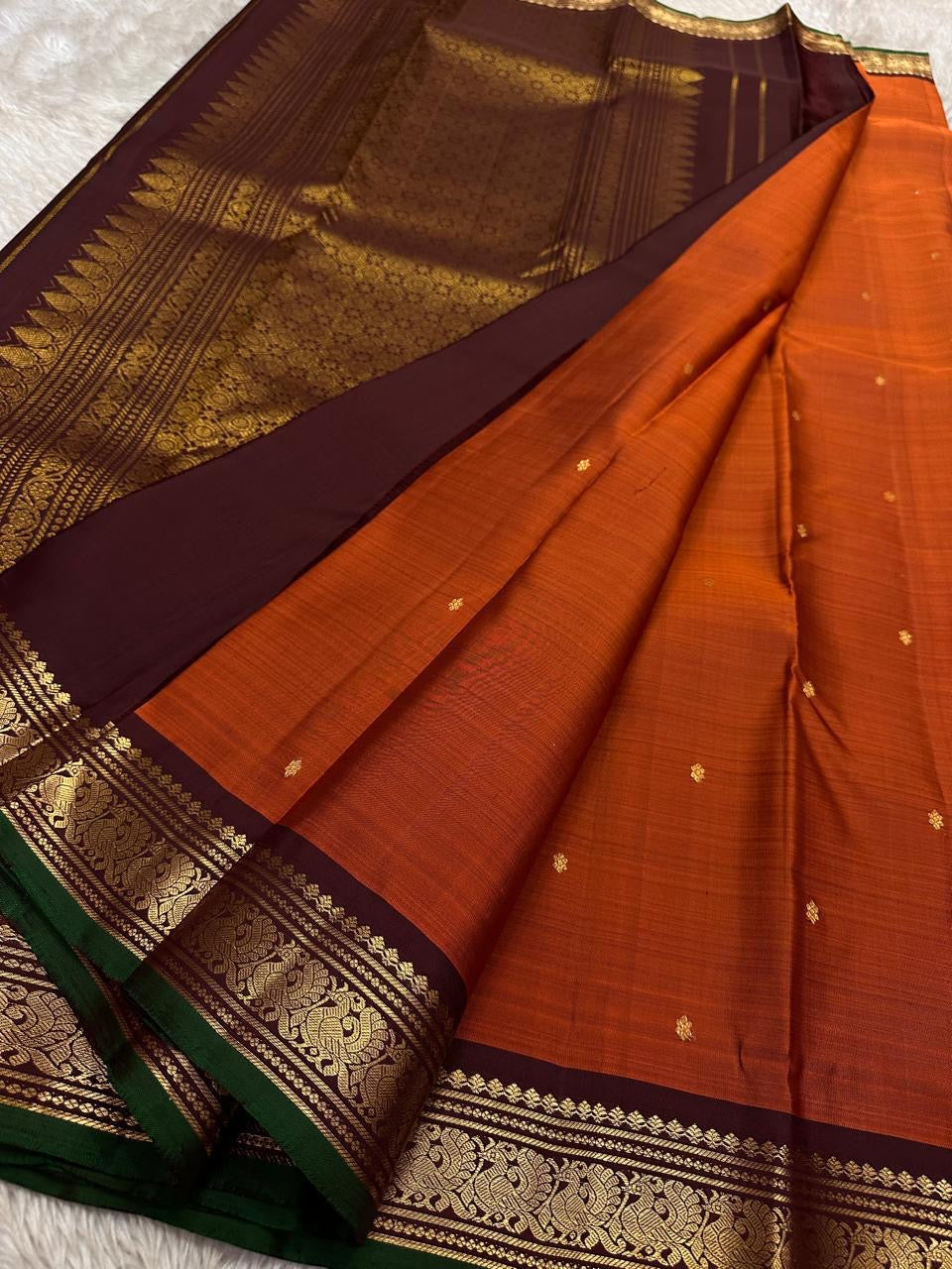 Saree spread open with rust orange body, tiny zari buttas, and a deep maroon pallu featuring dense zari woven patterning.