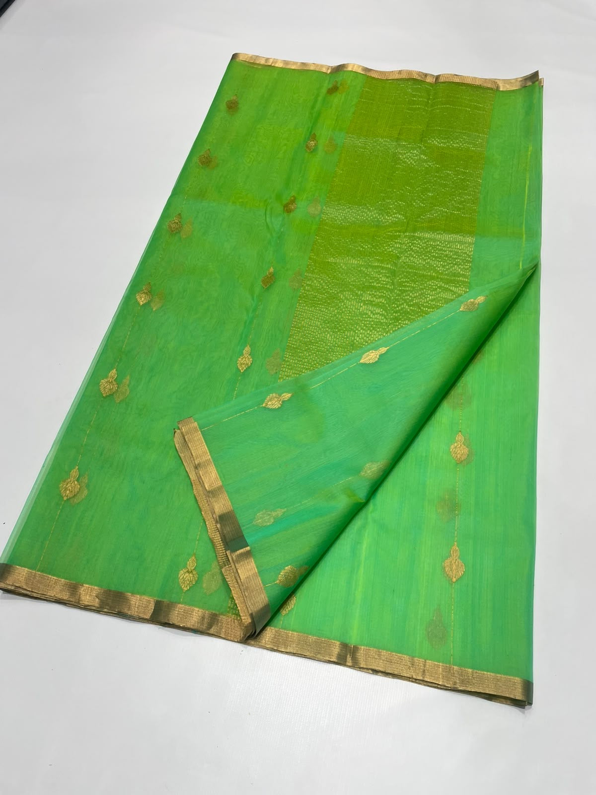 Sea glass green Katan silk Chanderi saree laid open showing gold-toned butis, narrow gold border and shimmering pallu