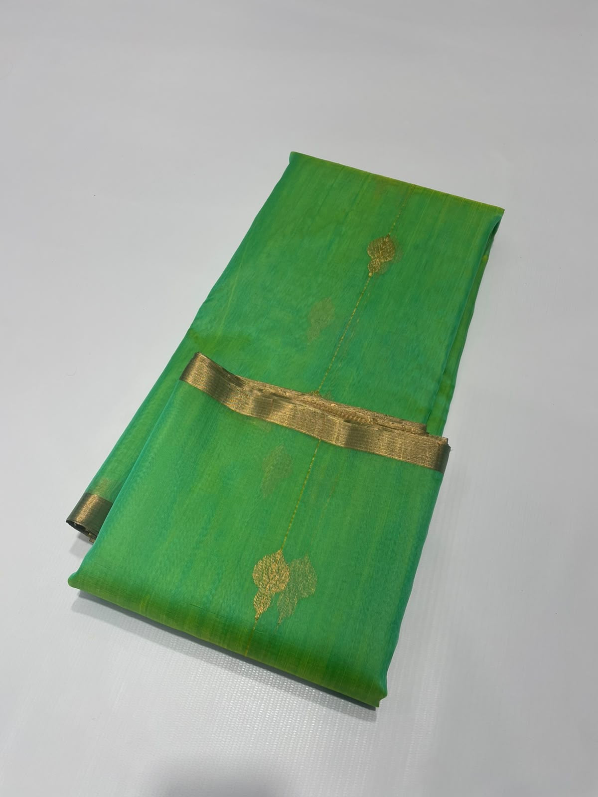 Folded sea glass green Katan silk Chanderi saree showing the narrow gold-toned border edge