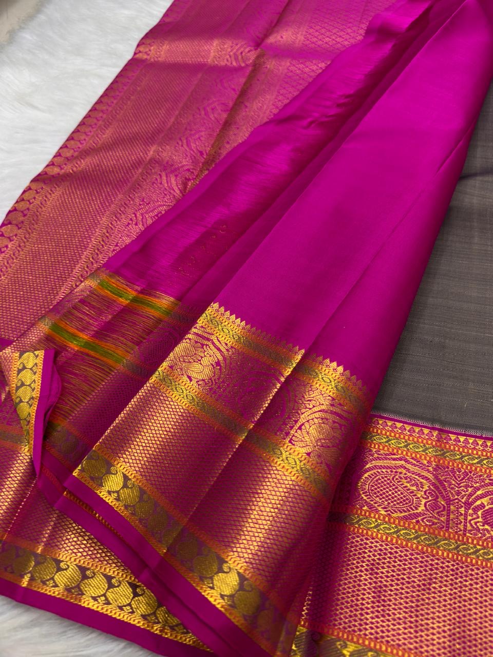 Folded Charcoal Grey Korvai saree highlighting statement gold zari butta and intricate Rani Pink border.