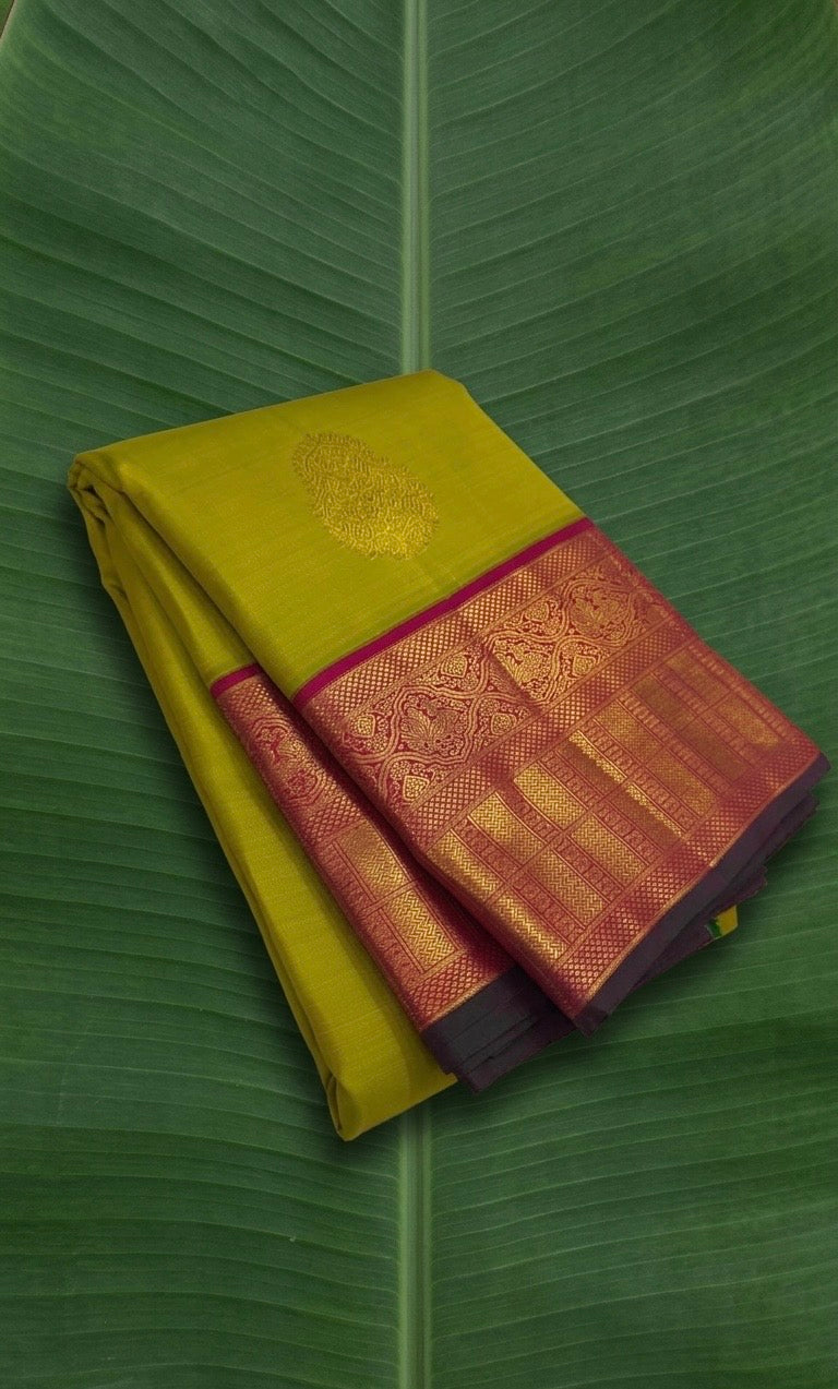 Chartreuse green handwoven Kanchi Pattu saree folded showing magenta Korvai border and flower butta body — Idam Living