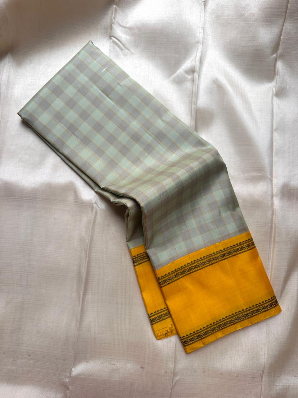 Grey and pale green checked Kanchipuram silk saree folded with mustard zari border on white fabric