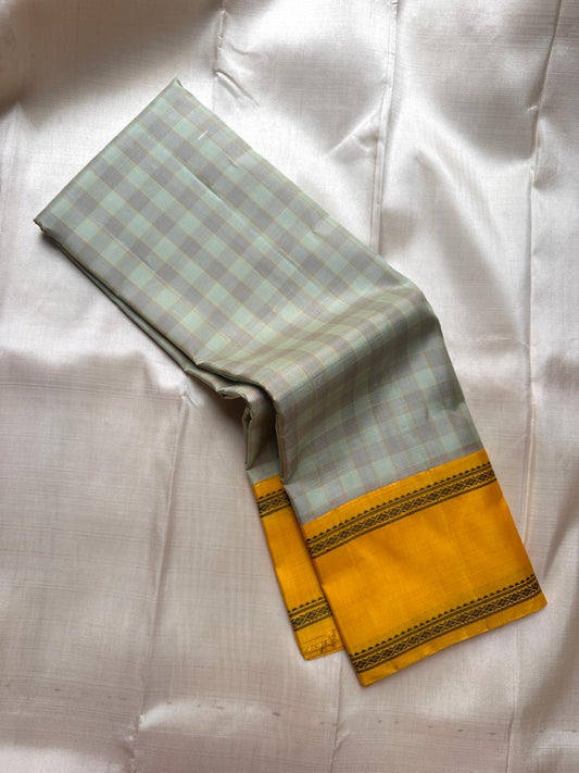 Grey and pale green checked Kanchipuram silk saree folded with mustard zari border on white fabric