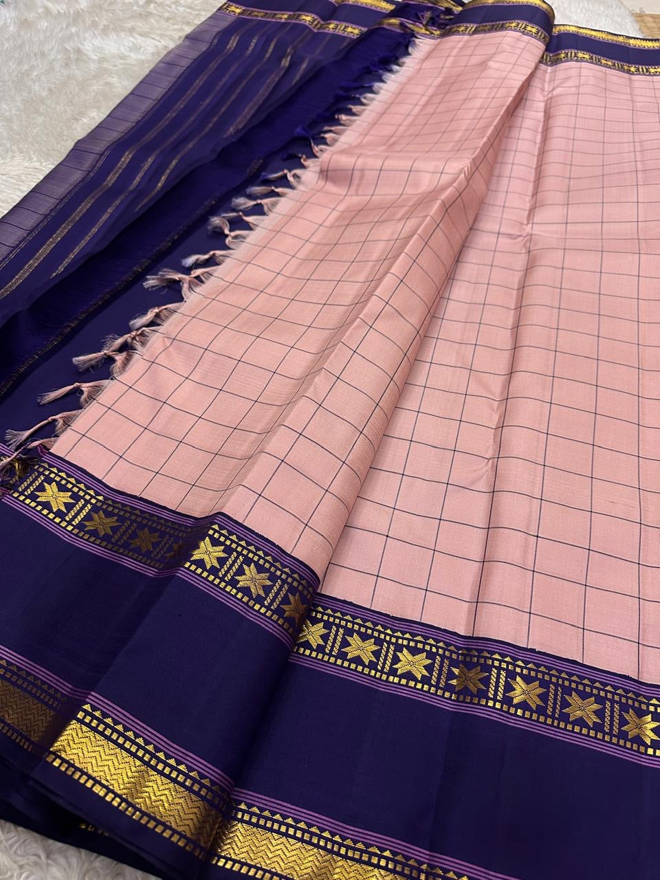 Full spread blush pink checked pure Kanchipuram silk saree with deep navy border, tassels, and gold zari detailing along the edg