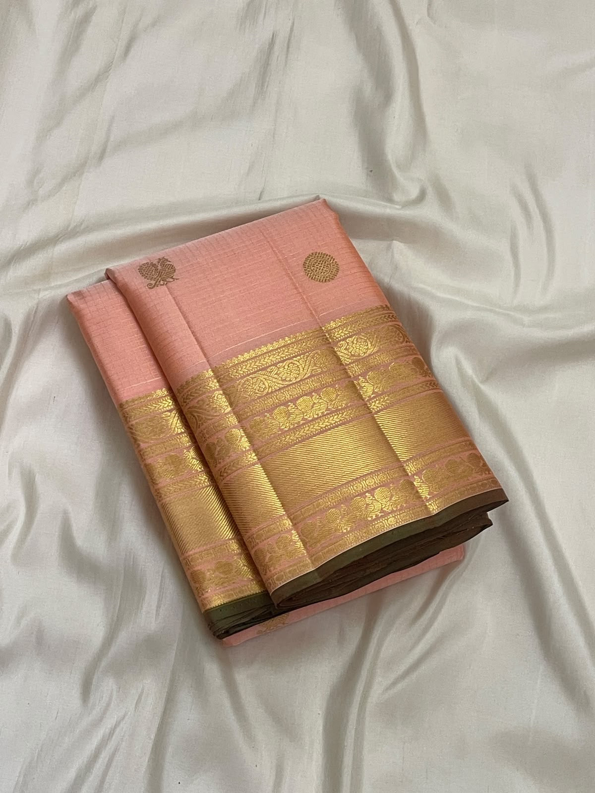 Tonal peach-pink border with layered classic-gold zari, geometric bands and small floral / leaf-like details.
