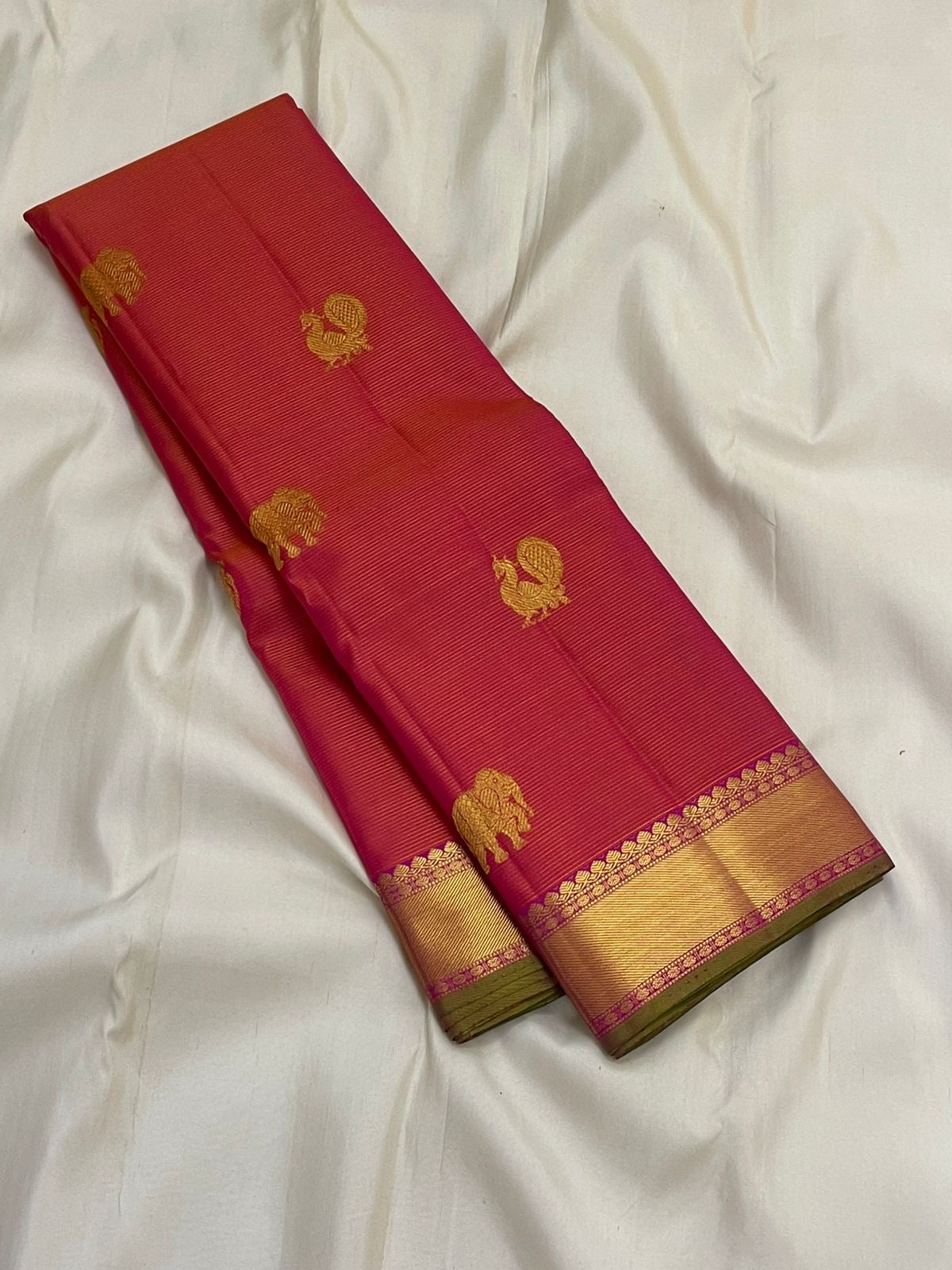 Long folded rani pink vairaoosi Kanchipuram silk saree showing gold zari buttas and wide zari border with green selvedge