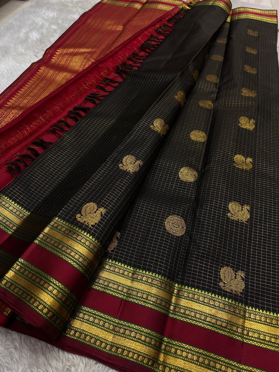 Folded black Kanchipuram silk saree with antique gold zari checks and maroon border