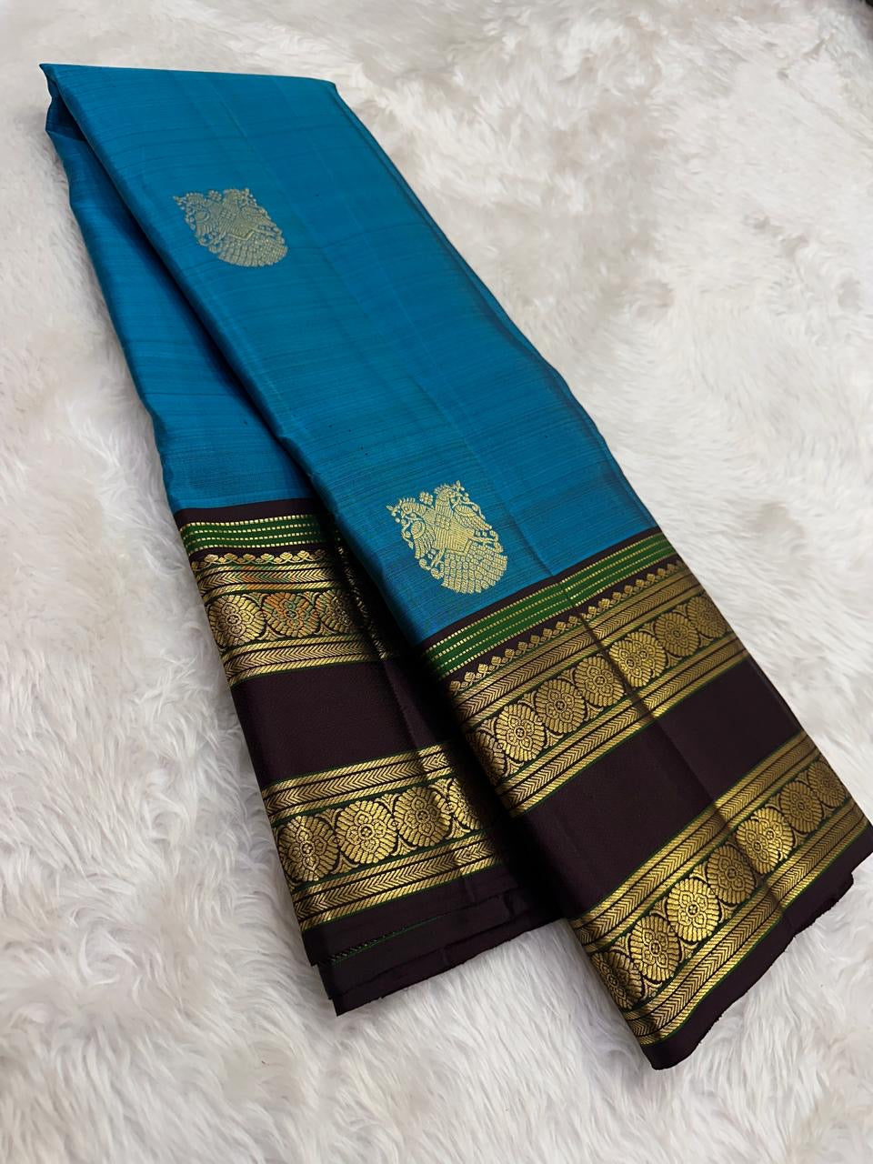 Coffee-brown rettapet border with green highlights on the turquoise blue saree.