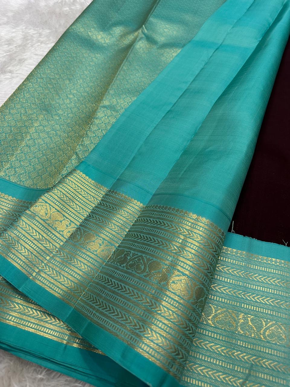 Folded coffee-brown Kancheepuram silk with small gold buttas and a contrasting fresh turquoise zari border.