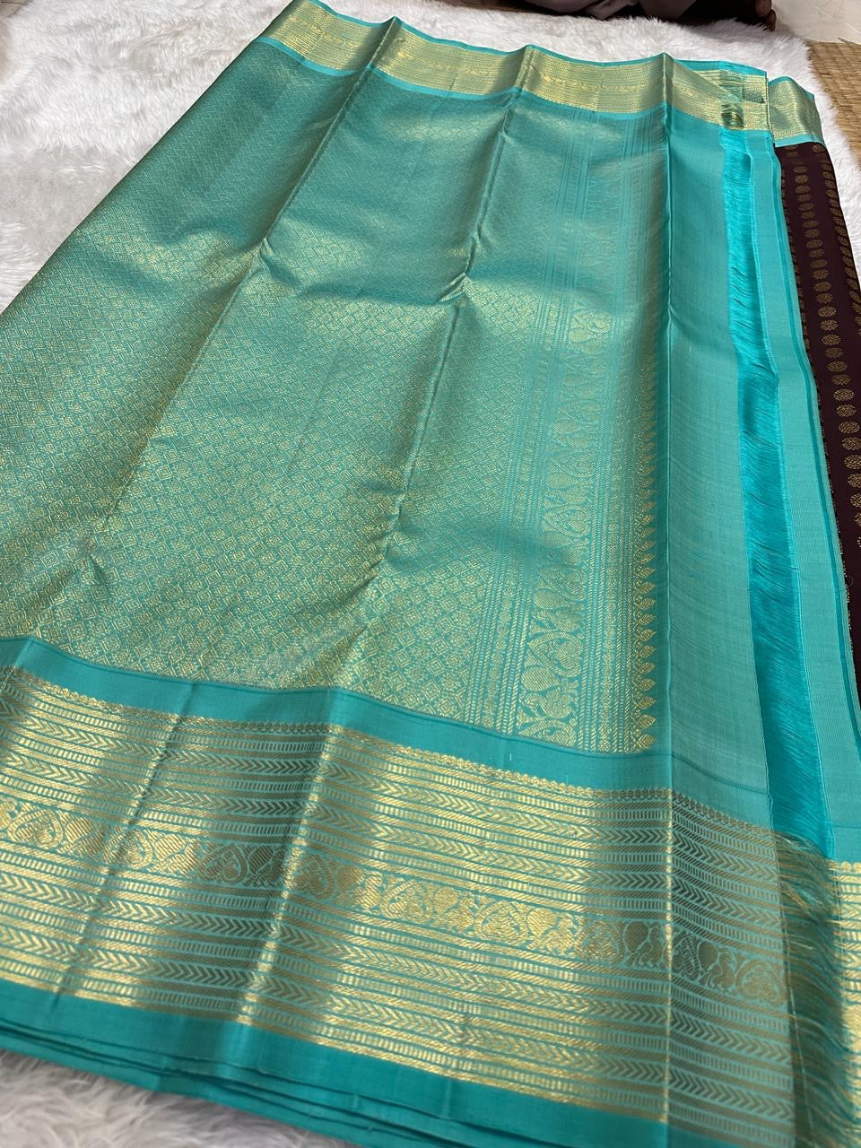 Opened coffee-brown silk body showing alternating gold kamalam and peacock buttas beside the turquoise border.