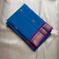 Folded teal blue Pure Kanchipuram silk saree with small zari buttas and a purple zari woven border with gold detailing.