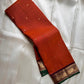 Folded rust orange Pure Kanchipuram silk saree showing small zari buttas and a maroon zari woven border with green contrast edging.