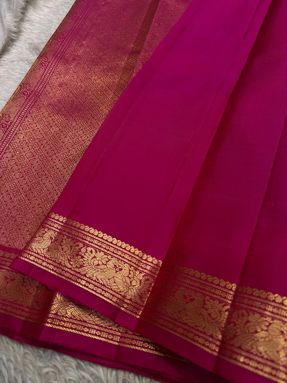 Close-up of magenta zari woven pallu with dense gold pattern and matching zari woven border on silk saree.