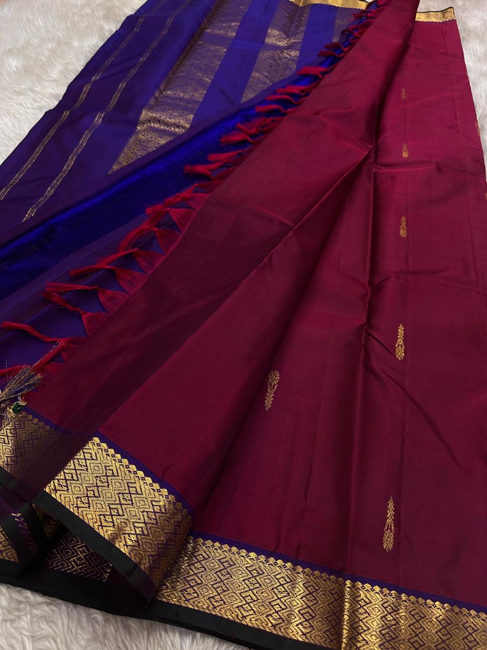 Maroon Pure Kanchipuram silk saree spread with zari buttas and a contrasting royal blue pallu section with tassels.