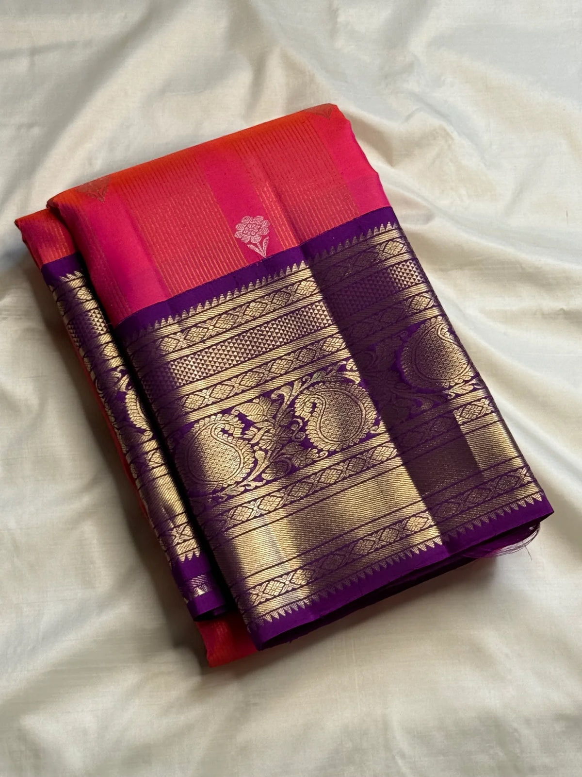 Handwoven coral silk body shifting toward amethyst with a deep violet contrast Kanchipuram border.