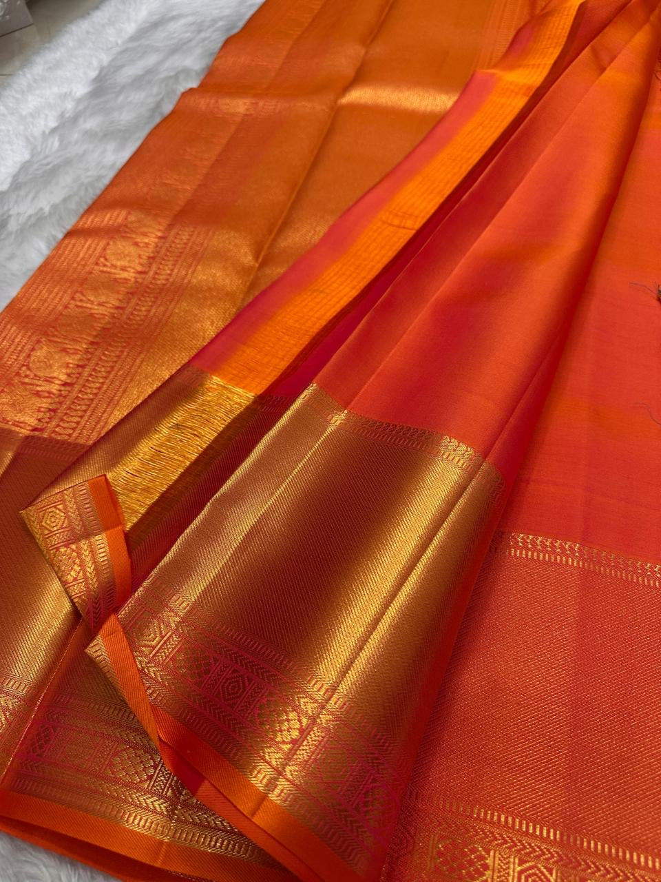 Dense gold zari buttas creating a jaal-like ornamental effect across the coral-red Kanchipuram silk.