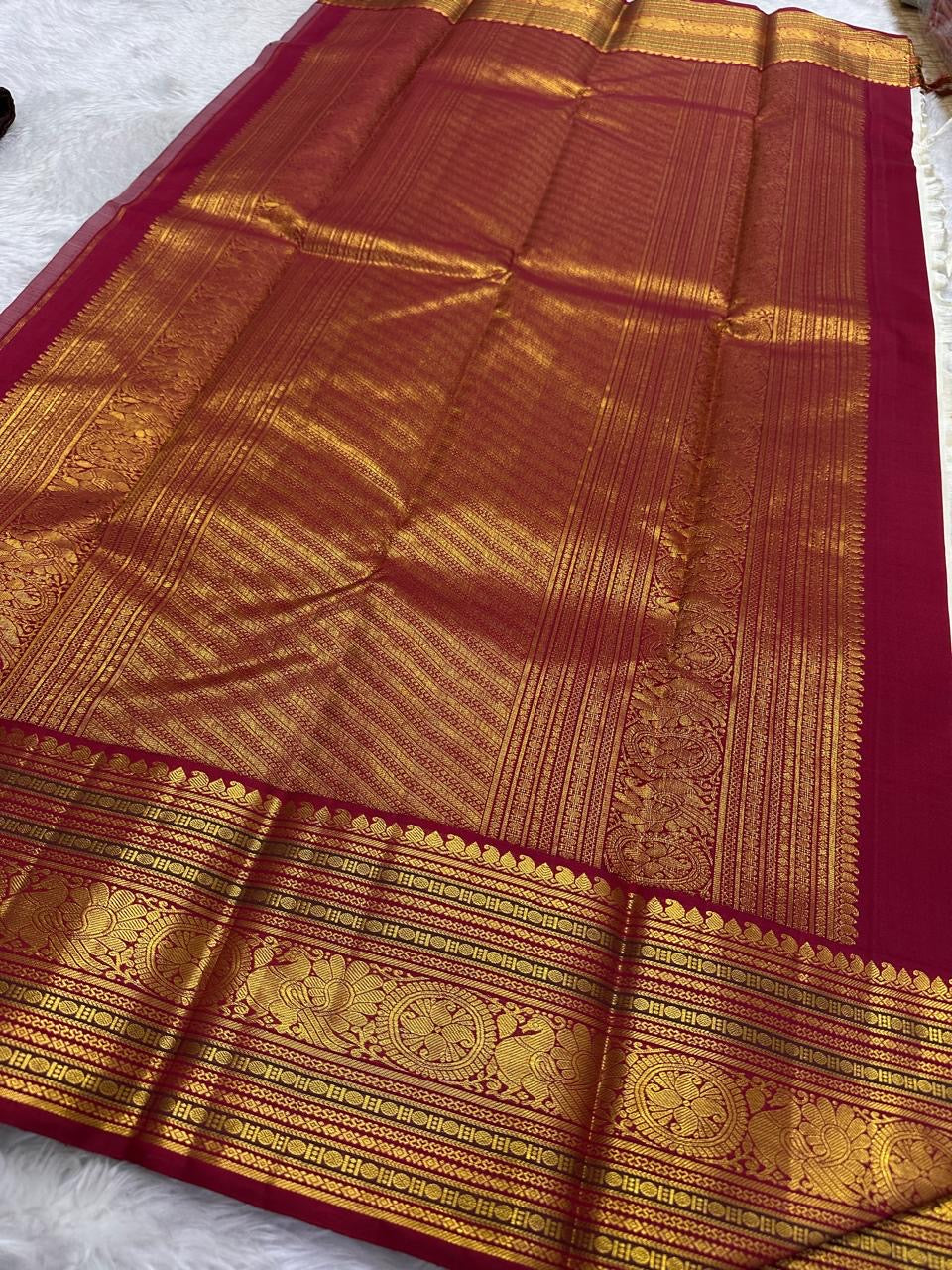 Close view of warm ivory silk meeting a deep red Korvai border with stylised bird and circular medallion forms.