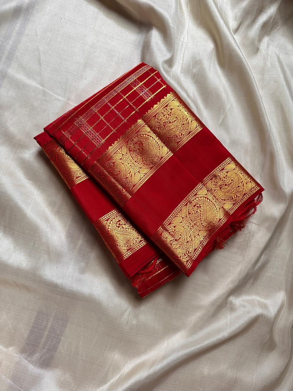 Folded Crimson Red Pure Silk Kanchipuram Zari Kattam saree with a large ornamental gold zari Sorgavasal Mayil and Manga border.