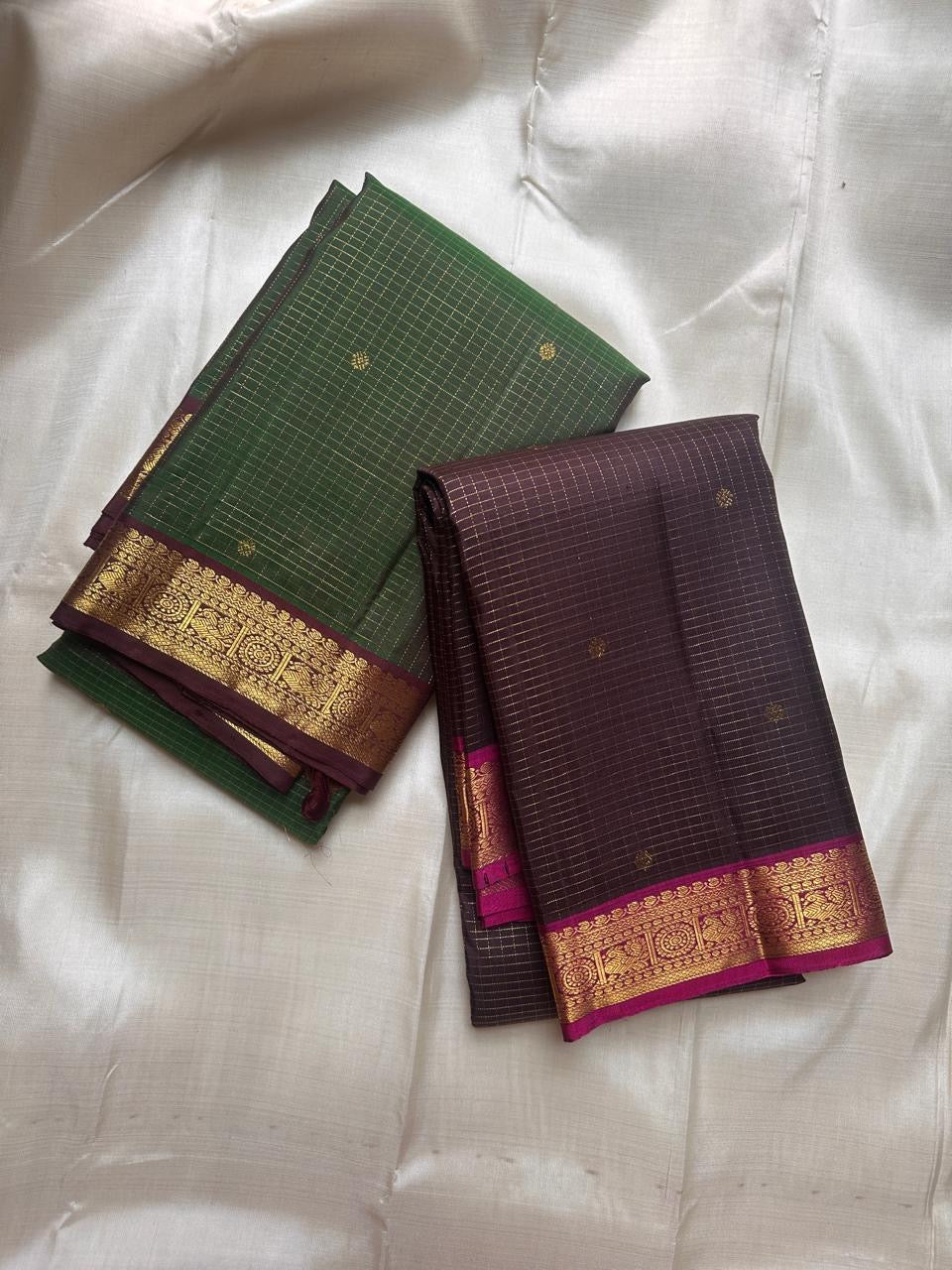 Two folded pure Kanchipuram silk sarees in green and deep brown with zari borders on beige backdrop
