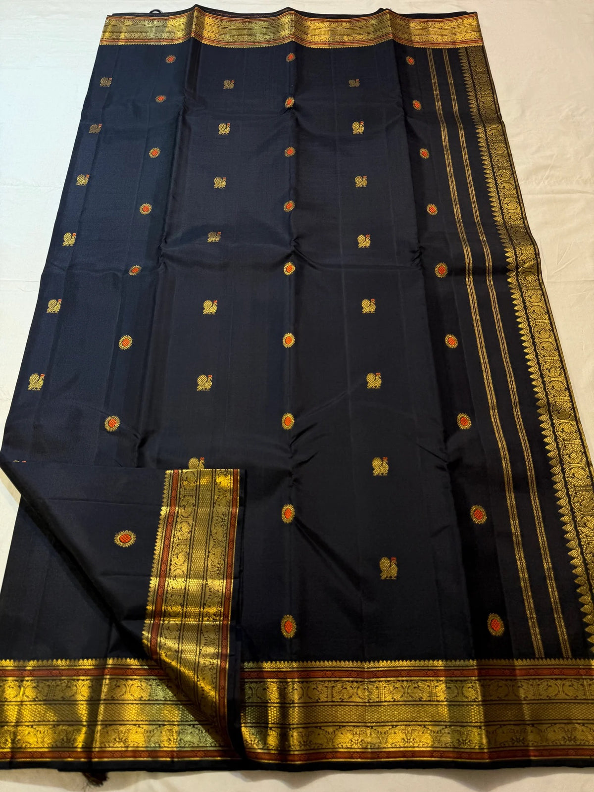 Close view of black silk with spaced meenakari buttas and a broad classic-gold border.