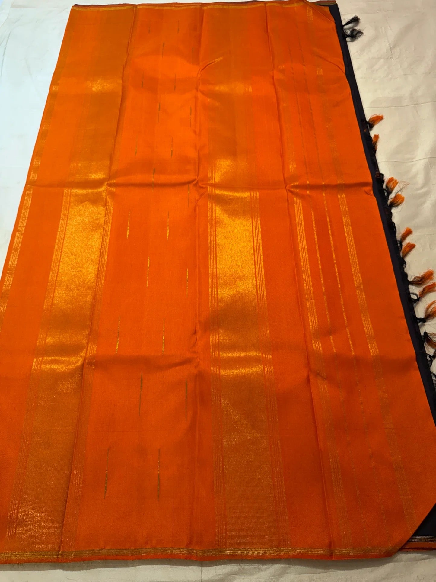 Folded Kanchana Brownish Purple saree showing narrow orange and gold zari edge.