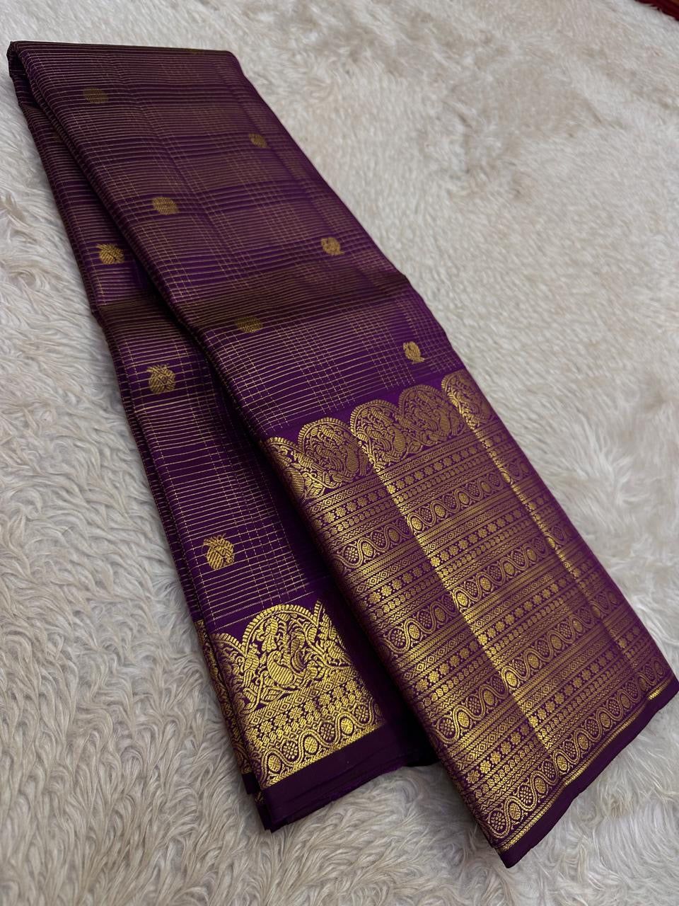 Folded Deep Aubergine Purple Pure Silk Kanchipuram saree showing fine gold Kattam lines and elaborate zari border.