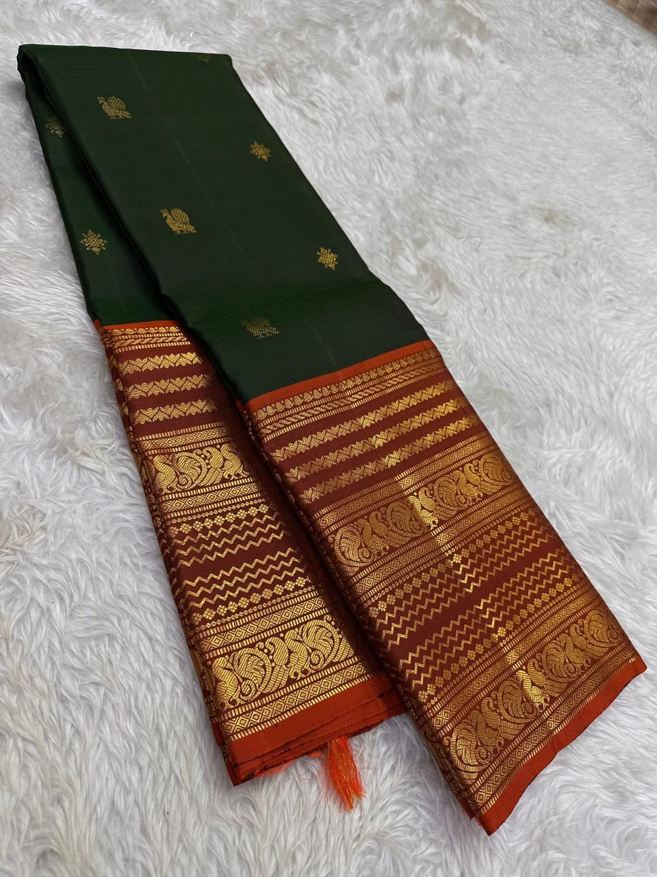 Rust orange pallu with red silk thread motifs on deep forest green Varisaipet saree
