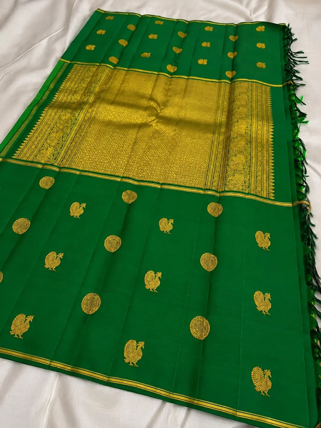 Folded deep green pure silk Kanjivaram Butta saree with traditional handwoven gold zari motifs.
