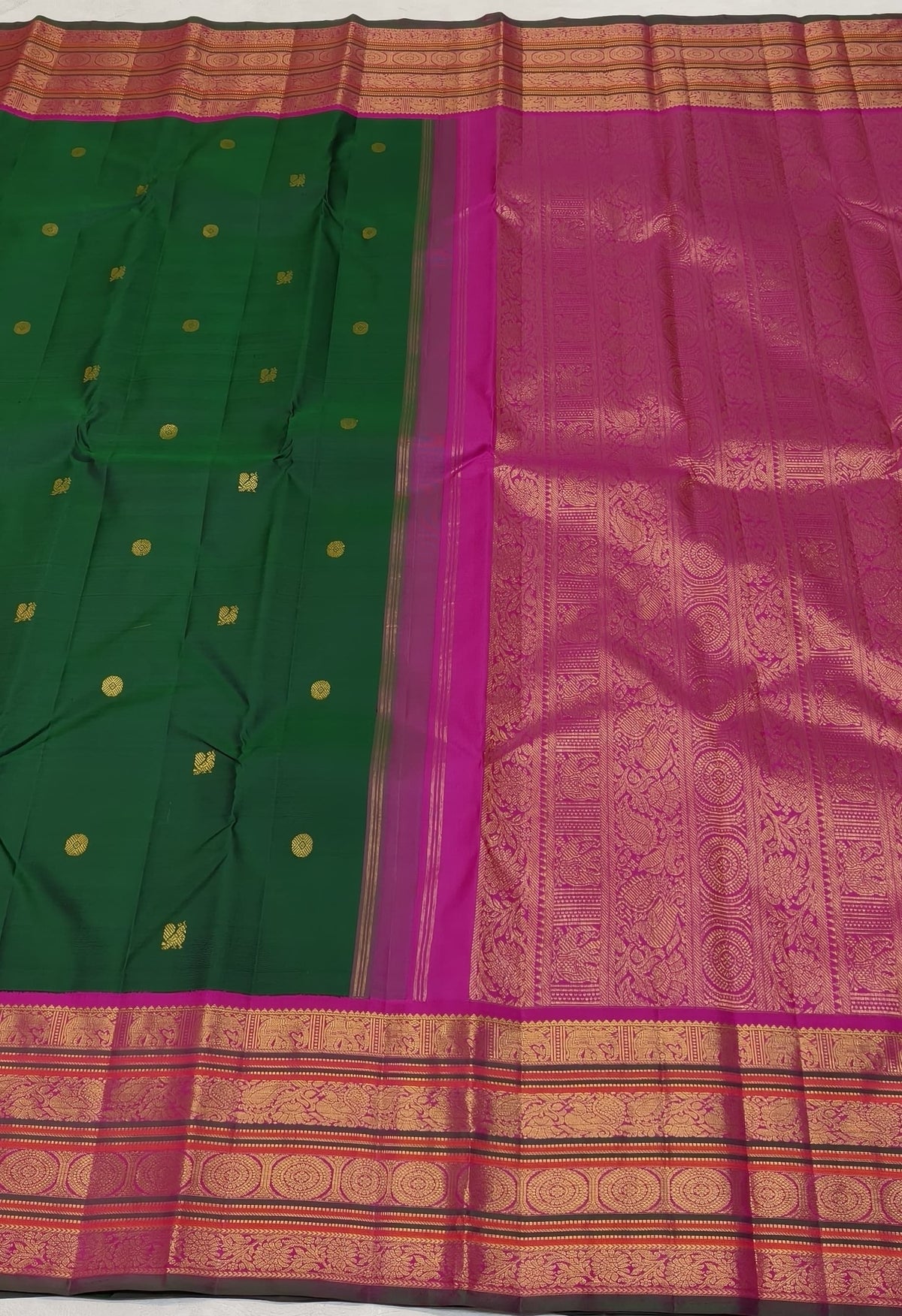 Deep green Kanjivaram saree showing its contrasting magenta border and elaborate gold zari ornamental registers.