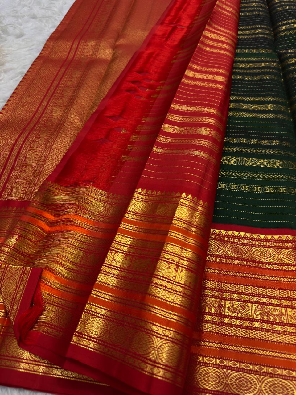 Detail of the saree border: A broad red to orange-red Varisaipet border built in repeated zari bands, with dense traditional geometric and figurative ornament arranged in architectural layers.