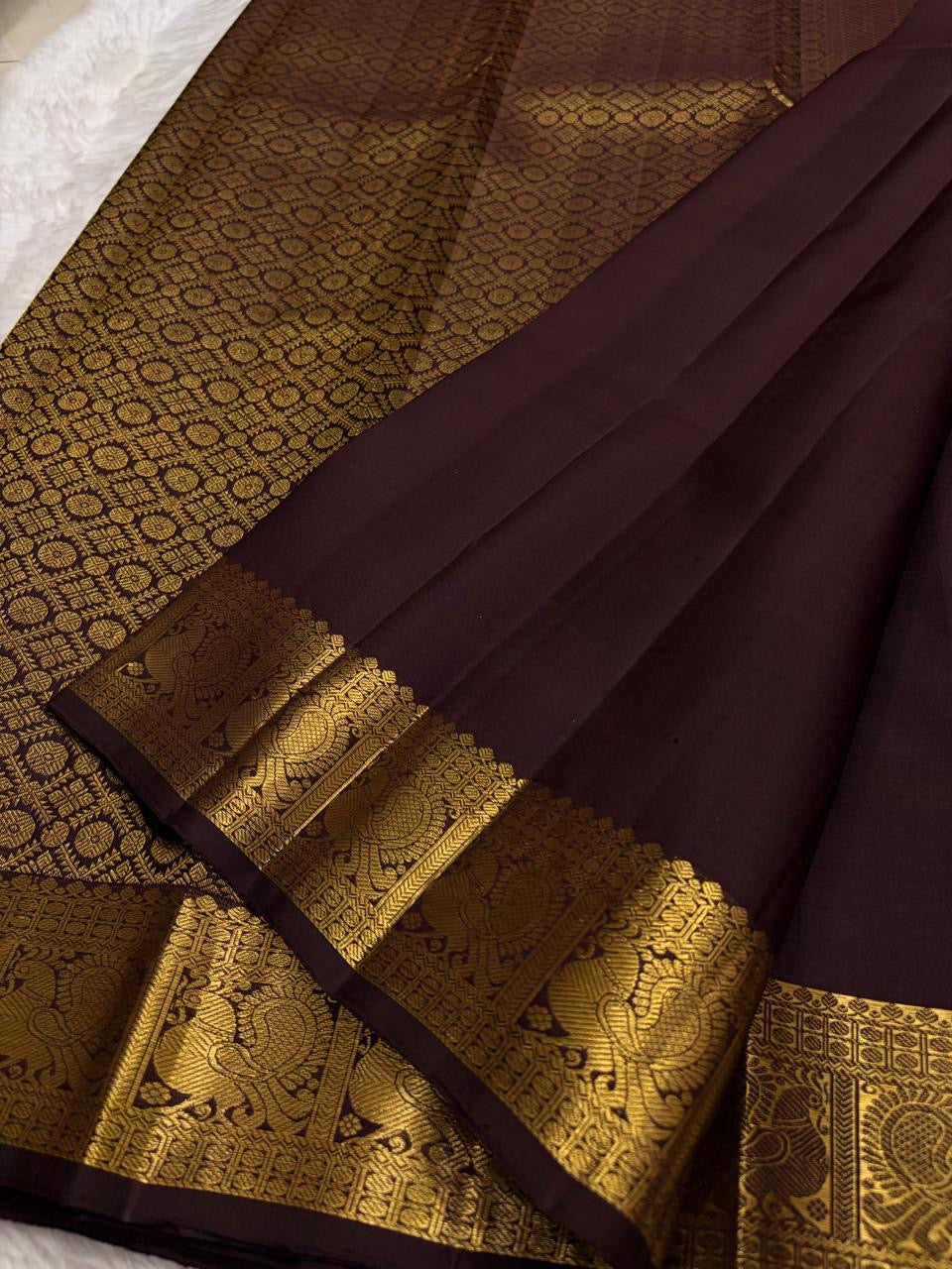 Dark brown Kanchipuram silk saree with small gold zari buttas and intricate Mayil border