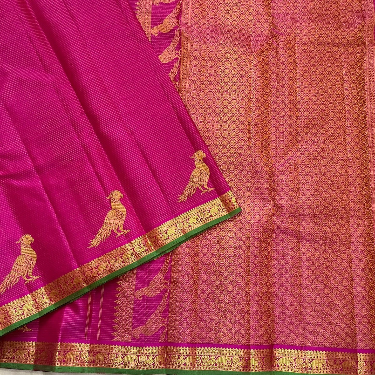 Folded deep magenta Kanchi Pattu pure silk saree showing Vairaoosi zari shimmer body and green contrast border