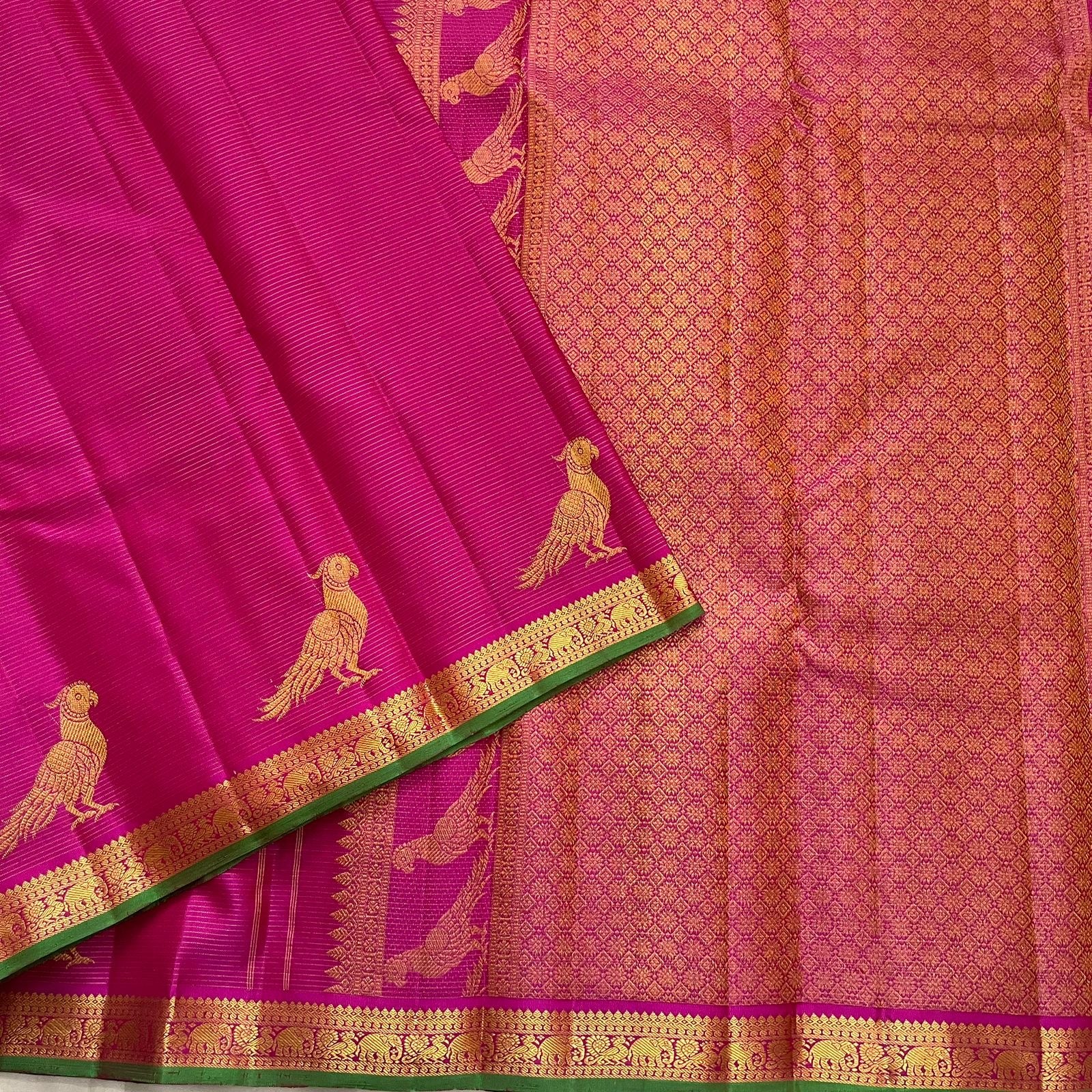 Folded deep magenta Kanchi Pattu pure silk saree showing Vairaoosi zari shimmer body and green contrast border