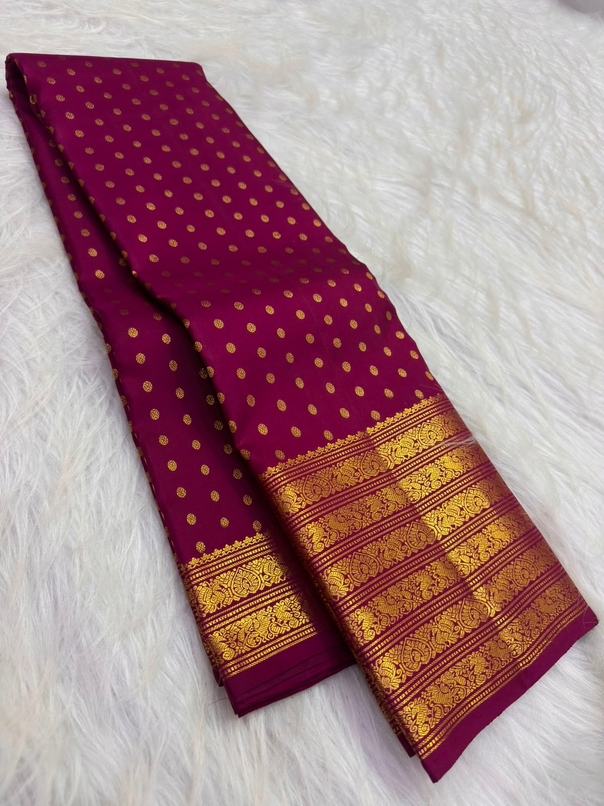 Folded deep cherry red Kanjivaram silk saree with evenly spaced circular gold zari buttas and an ornate border.