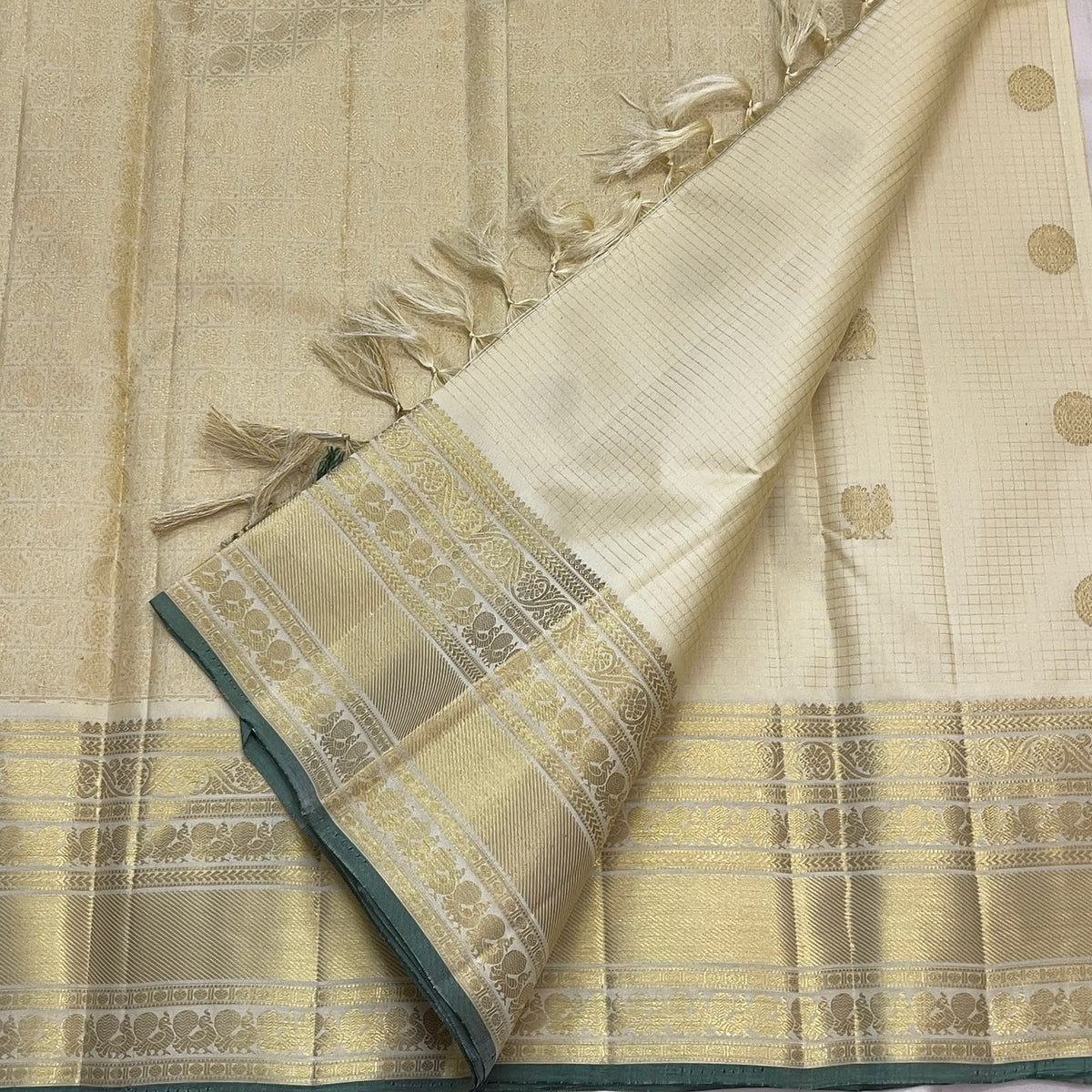 Warm ivory Kanjipuram silk saree with pale-gold zari kattam and green edging, folded view — Idam Living