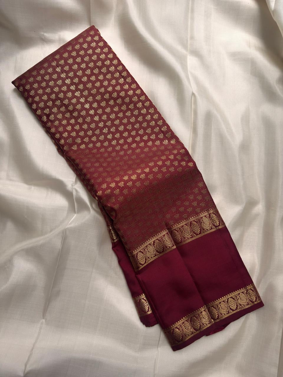 Dense antique-gold Kanchipuram pallu showing a fine geometric zari field against deep garnet silk.