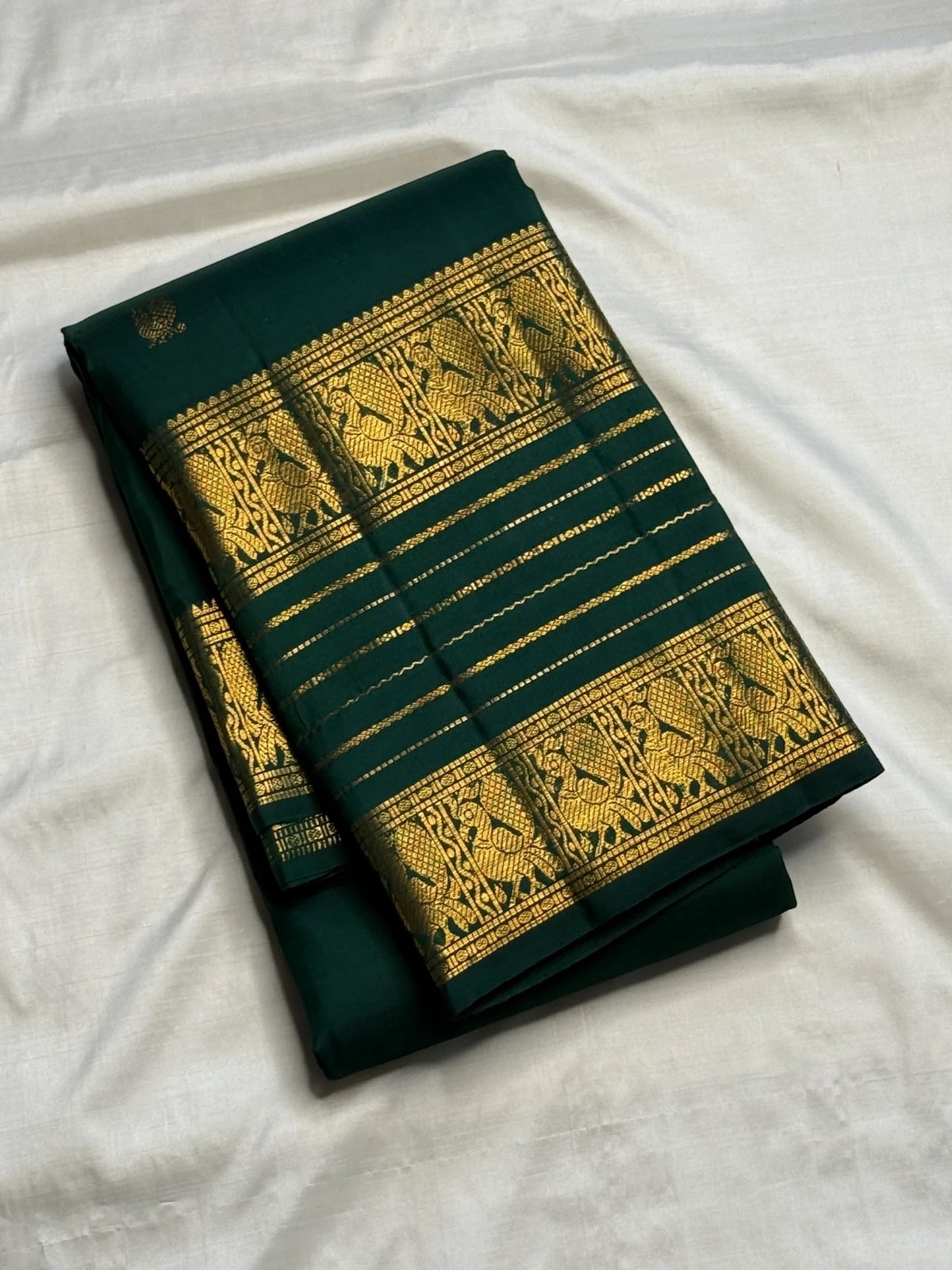 Deep green Kanchipuram silk saree with spaced gold zari buttas and layered Varisaipet border.