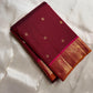 Folded deep red silk saree with small gold buttas and zari woven border on ivory fabric backdrop.