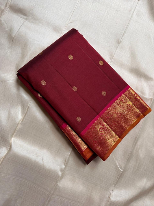 Folded deep red silk saree with small gold buttas and zari woven border on ivory fabric backdrop.
